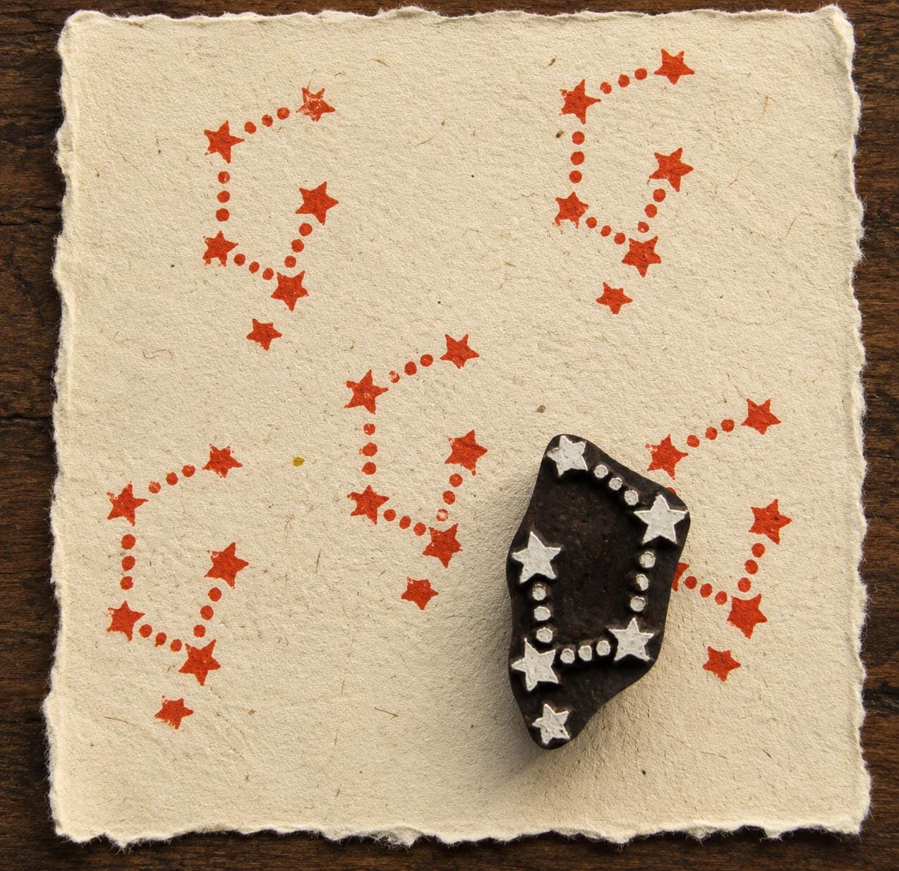 Hand-carved constellation star wooden printing block with connected red star impressions on handmade textured paper.