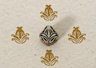 Hand carved Indian wooden textile printing block with a symmetrical stylised leaf and floral motif, shown with four ochre impressions on handmade paper.