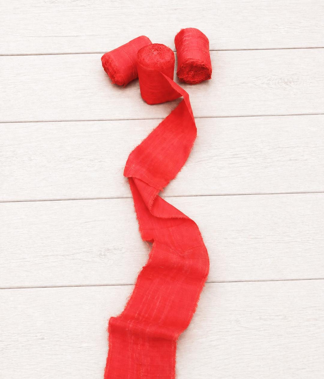 Extra wide vermilion recycled sari silk ribbon with three rolls and a flowing length displayed on a white wooden background.