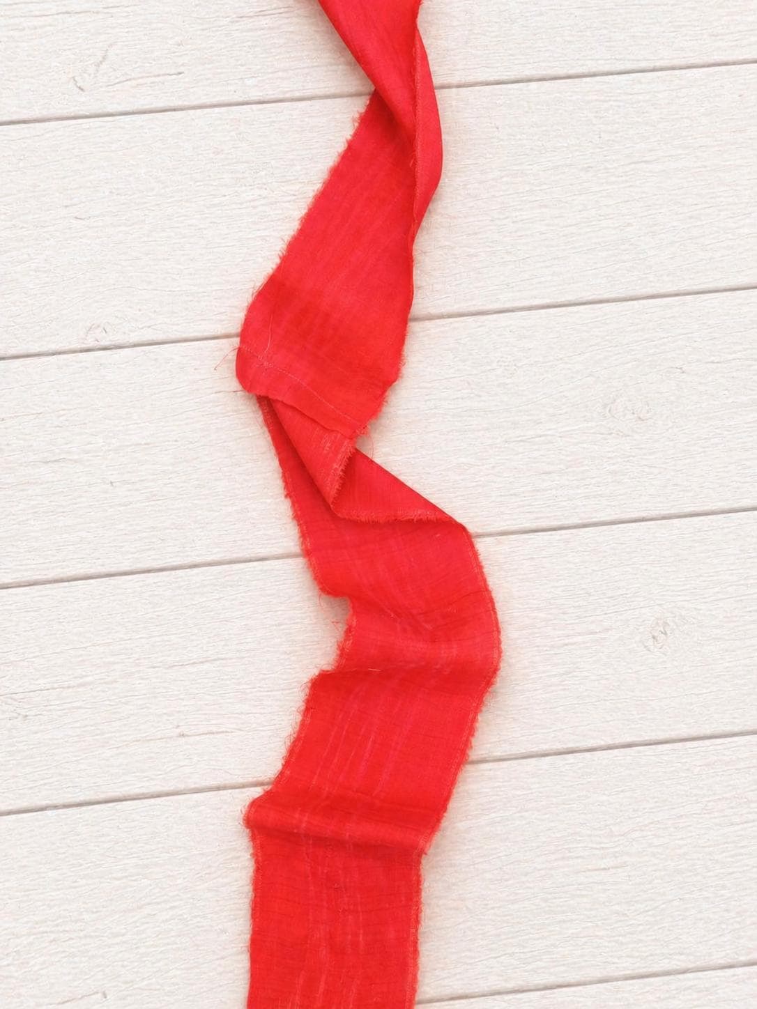 Close-up of wide vermilion recycled sari silk ribbon showing its soft drape, woven silk texture, and raw frayed edges.