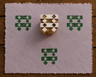 Hand carved wooden printing block featuring an interlocking diamond and band motif, shown with three green impressions on textured lavender handmade paper.