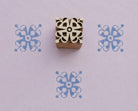 Hand carved wooden printing block featuring a symmetrical Ribbon Bloom motif with looping petals and rounded details, shown with three blue impressions on lavender handmade paper.