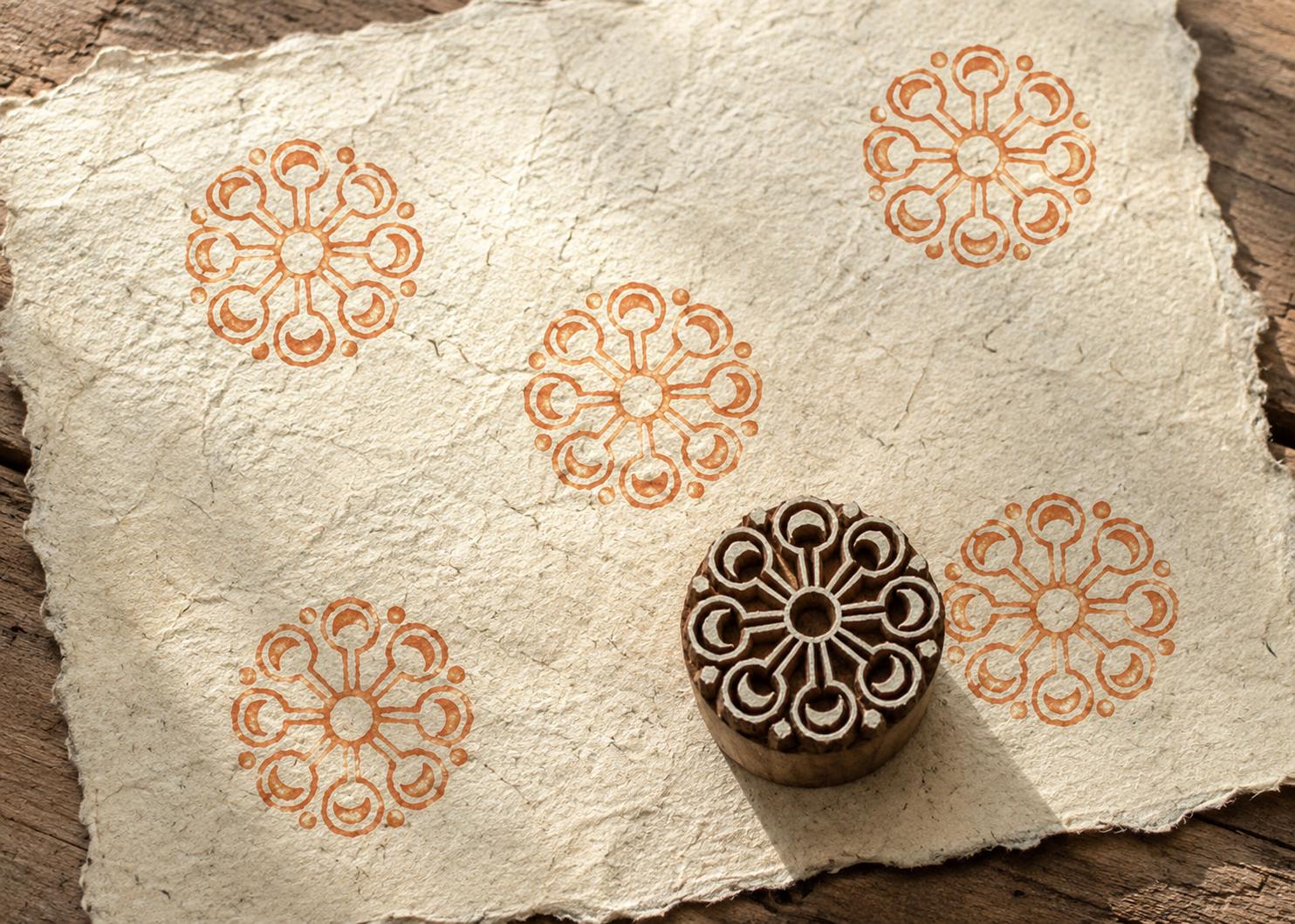 Hand-carved Crescent Sunwheel wood block stamp with warm terracotta circular medallion impressions on textured handmade paper.