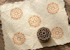 Hand-carved Crescent Sunwheel wood block stamp with warm terracotta circular medallion impressions on textured handmade paper.