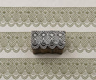 Hand-carved wooden printing block with an intricate diamond lattice and scalloped ornamental border, shown with repeated green impressions on textured handmade paper.