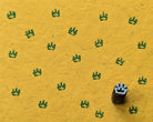 Small hand-carved wooden printing block with a crown motif beside repeated green crown impressions on handmade yellow paper.