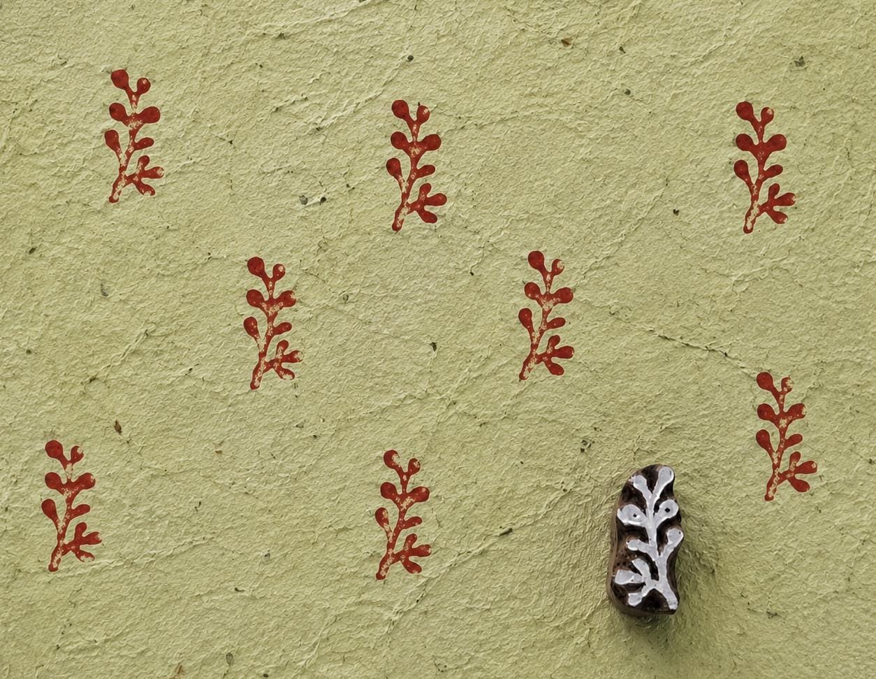 Hand carved wooden printing block measuring approximately 2.7 × 1.6 cm, featuring an unusual coral-like branching motif, shown with repeated red impressions on textured handmade paper.