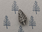 Hand carved bare tree wooden block stamp displayed on textured handmade paper with repeated blue tree impressions.