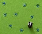 Hand carved heart sunburst wood printing block shown on green handmade paper with repeated blue heart prints