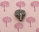 Hand carved leafy canopy wooden printing block surrounded by repeated botanical tree impressions on textured pink handmade paper.