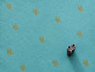 Hand-carved wooden three-leaf sprig printing block beside repeated ochre leaf impressions on textured turquoise handmade paper.