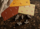 Set of five tiny hand carved wooden botanical printing blocks displayed on a distressed wooden surface with handmade paper samples showing their printed designs.