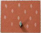 Tiny hand carved wooden leaf printing block, shown with repeated white leaf impressions on terracotta handmade paper.