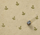 Tiny hand carved wooden printing block with a three-leaf sprout motif, shown with repeated olive green impressions on textured handmade paper