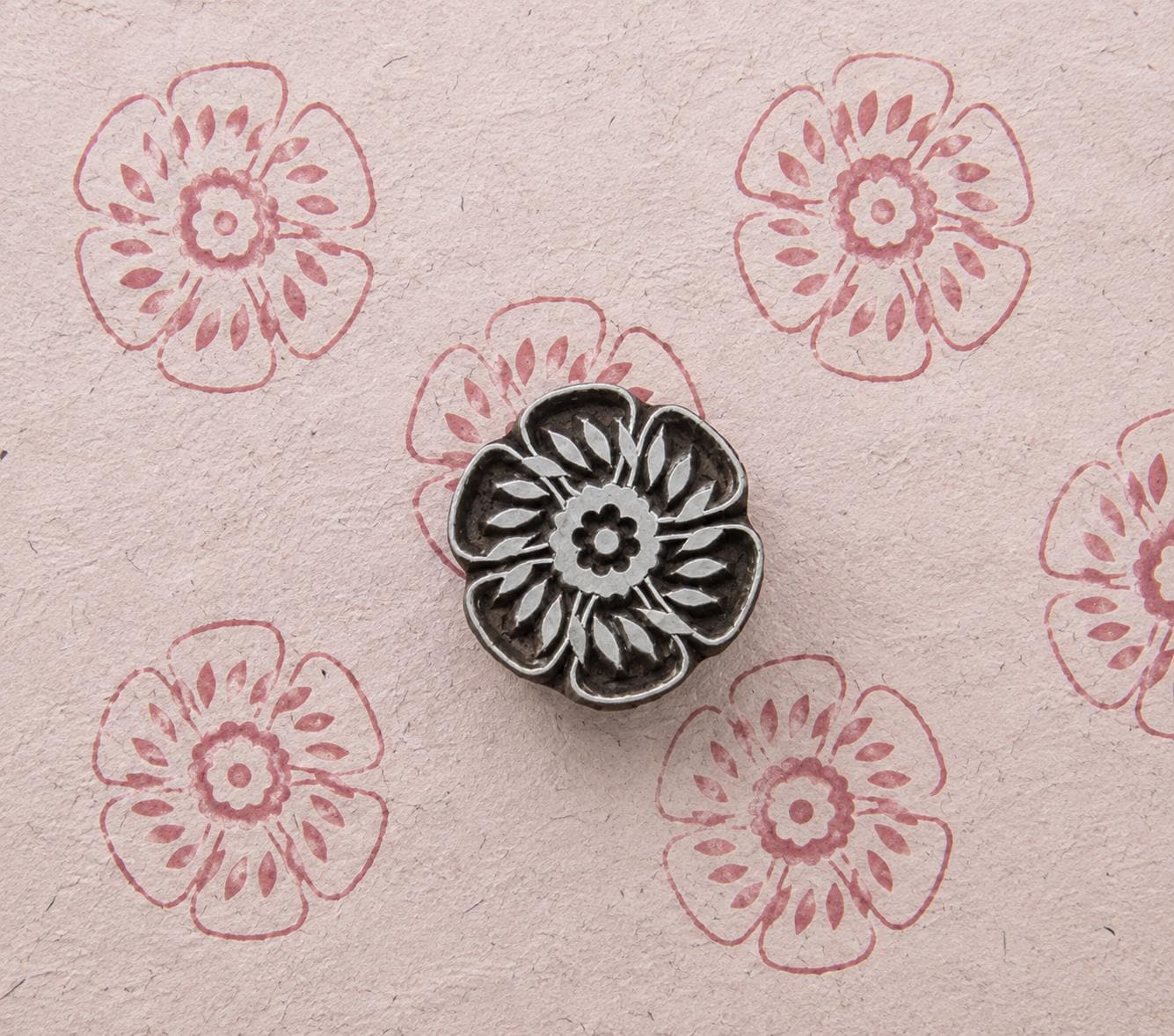 Hand carved wooden Garden Rosette stamp shown with repeated pink floral impressions on handmade paper.