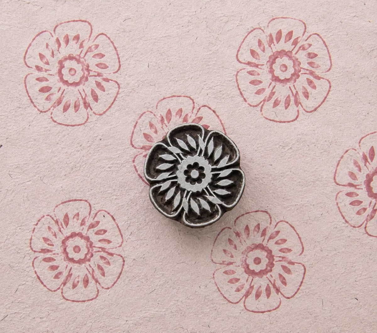 Hand carved wooden Garden Rosette stamp shown with repeated pink floral impressions on handmade paper.