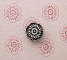 Hand carved wooden Garden Rosette stamp shown with repeated pink floral impressions on handmade paper.