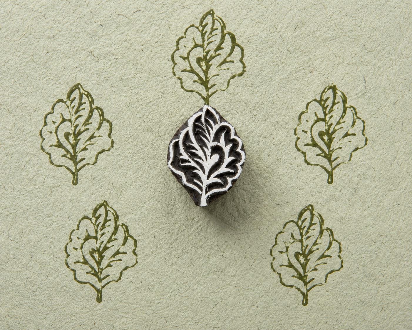 Hand carved wooden oak leaf stamp shown with repeated green leaf impressions on textured handmade paper.