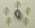 Hand carved wooden oak leaf stamp shown with repeated green leaf impressions on textured handmade paper.