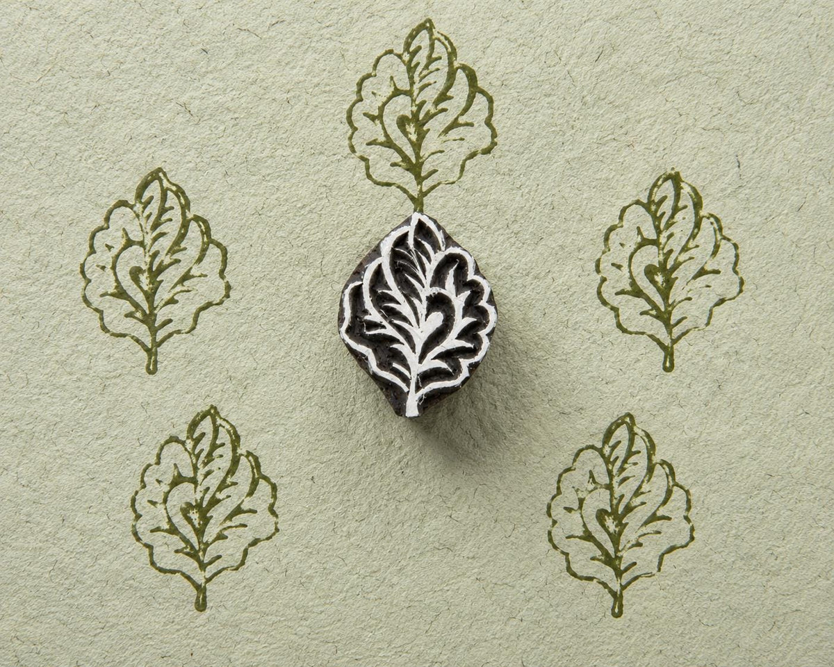 Hand carved wooden oak leaf stamp shown with repeated green leaf impressions on textured handmade paper.