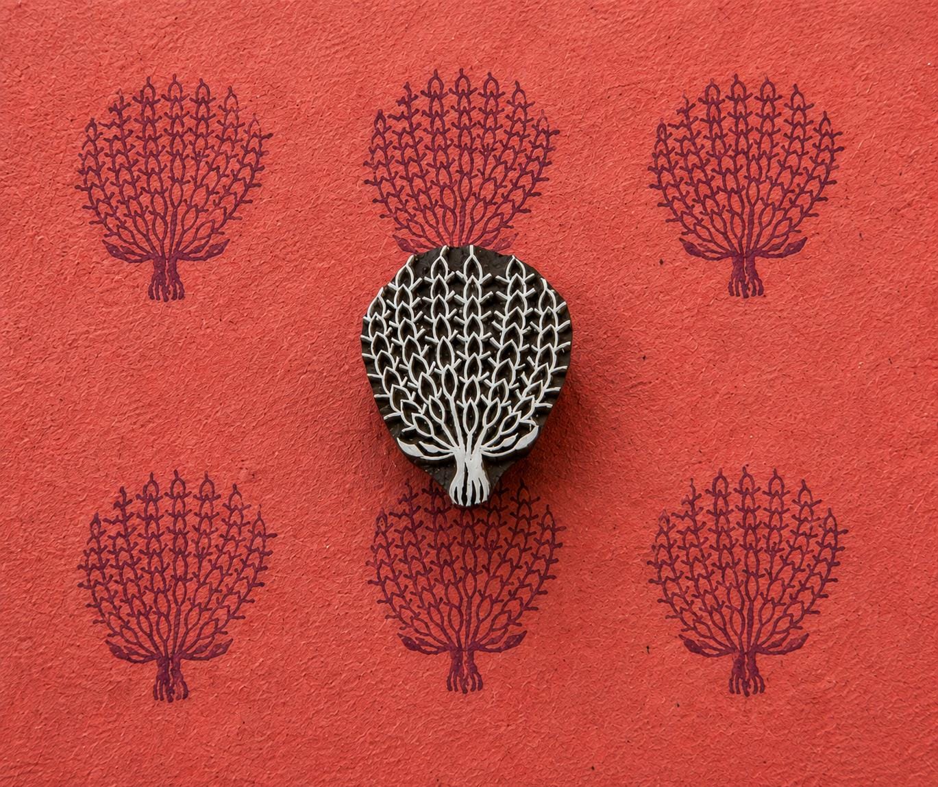 Hand carved wooden Lace Tree stamp shown with repeated dark purple tree impressions on textured red handmade paper.
