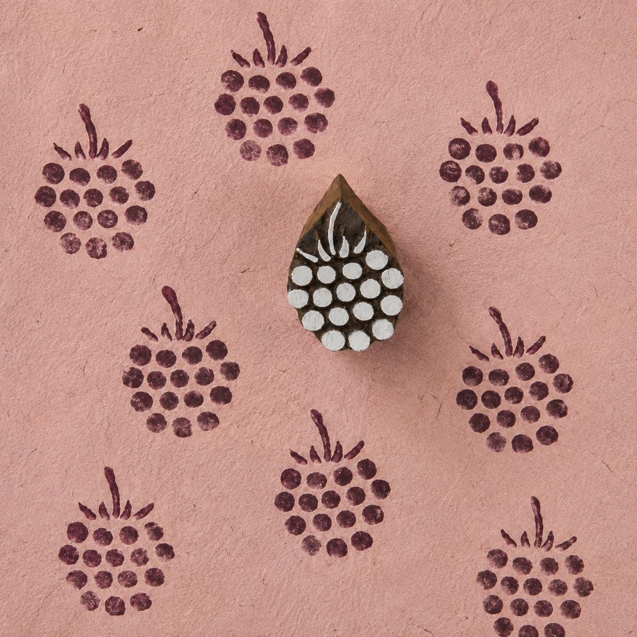Hand-carved wooden Berry Cluster stamp shown with repeated burgundy botanical impressions on textured pink handmade paper.