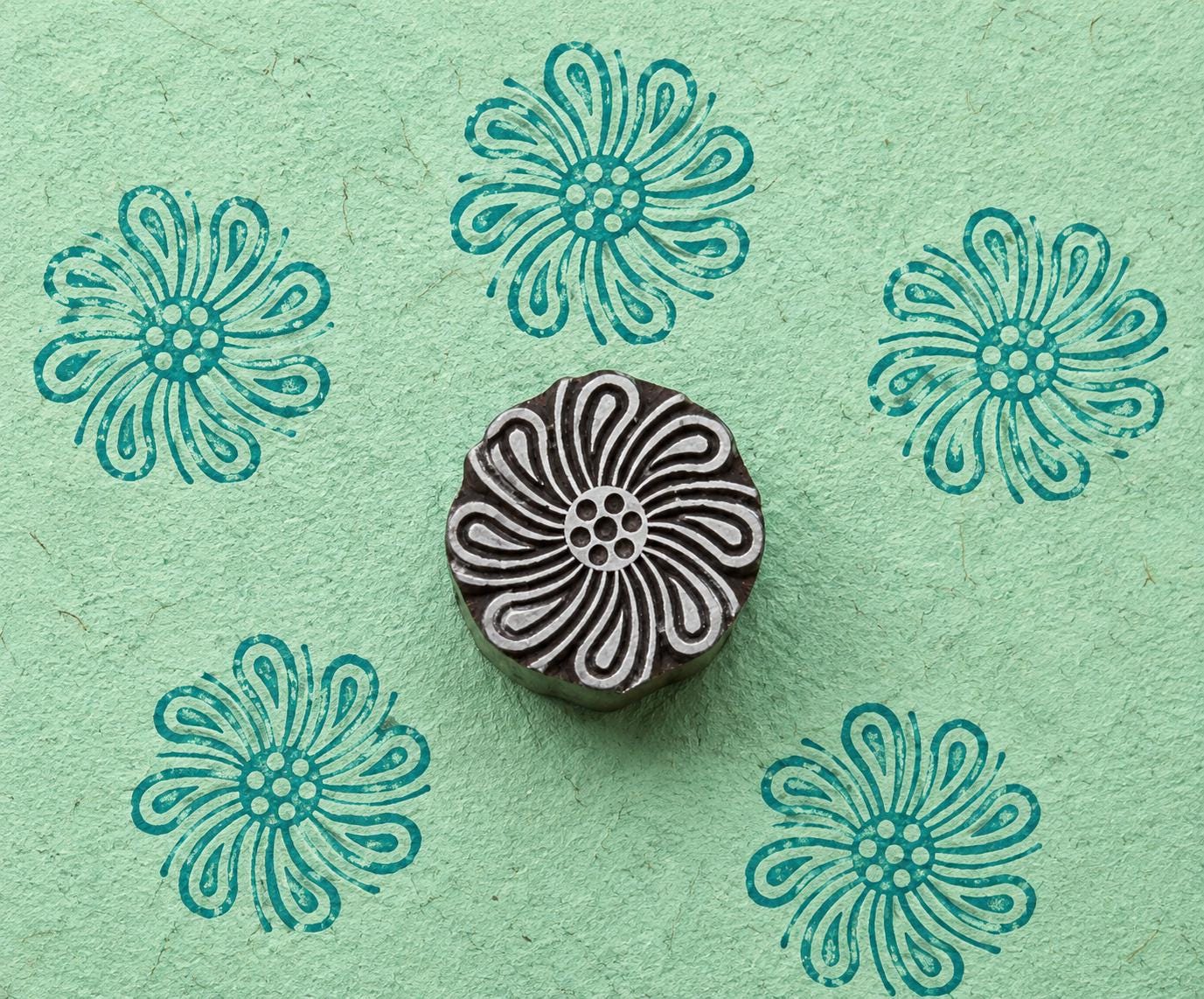 Hand-carved wooden Looped Petal Flower stamp shown with five teal impressions on textured mint green handmade paper.