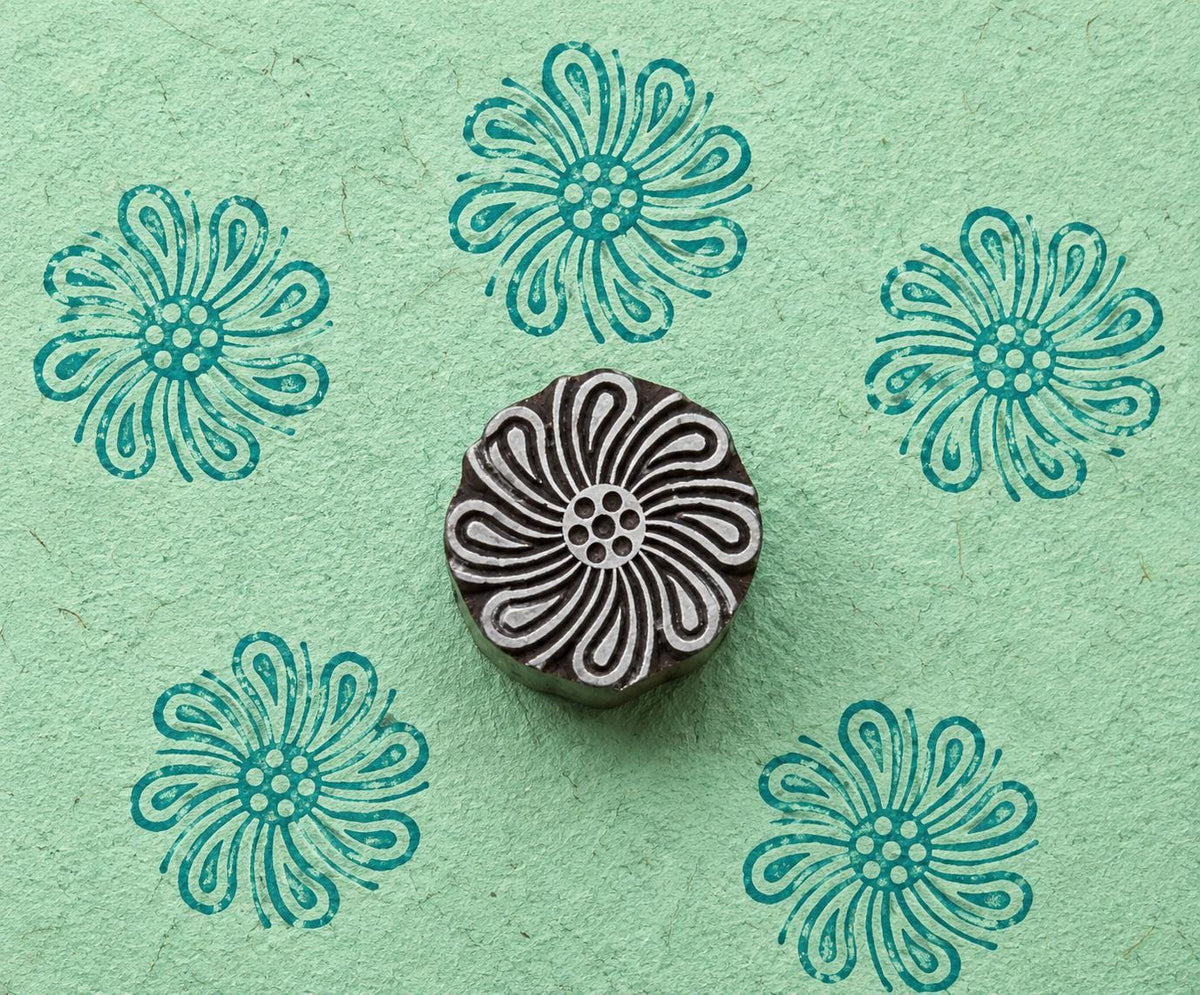 Hand-carved wooden Looped Petal Flower stamp shown with five teal impressions on textured mint green handmade paper.