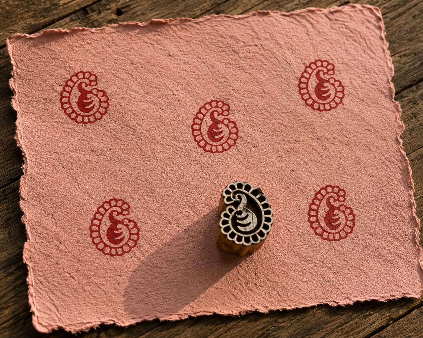 Hand carved Petite Paisley wood block stamp with deep red paisley print on handmade paper for fabric printing, pottery, clay and paper crafts.
