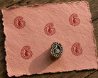 Hand carved Petite Paisley wood block stamp with deep red paisley print on handmade paper for fabric printing, pottery, clay and paper crafts.