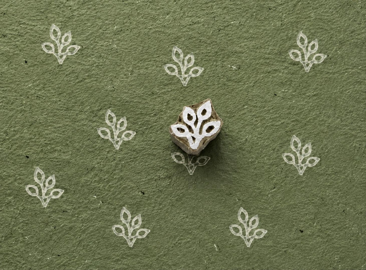Four Loop Leaf wooden stamp shown with repeated white impressions on textured green handmade paper.