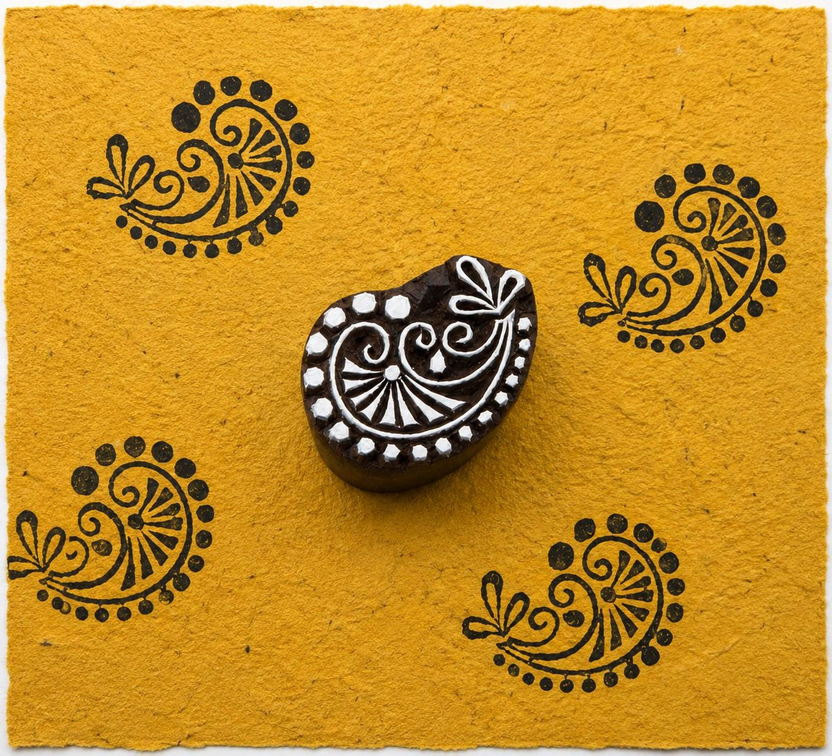 Floral vine paisley hand carved wooden printing block with repeated dark ink impressions on handmade mustard paper