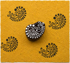 Floral vine paisley hand carved wooden printing block with repeated dark ink impressions on handmade mustard paper