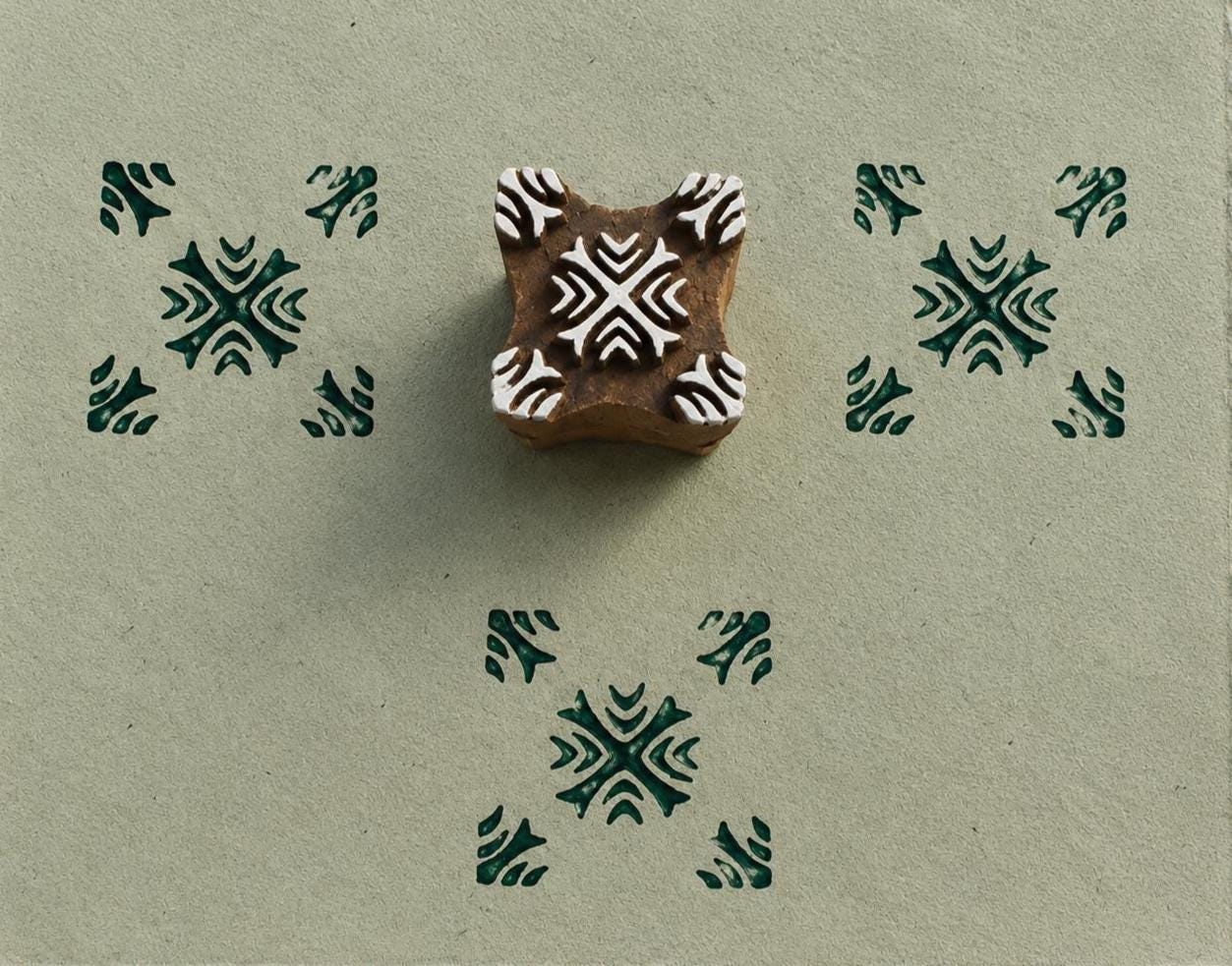 Hand carved Indian wooden printing block featuring a tribal cross geometric pattern with dark green impressions on handmade paper.