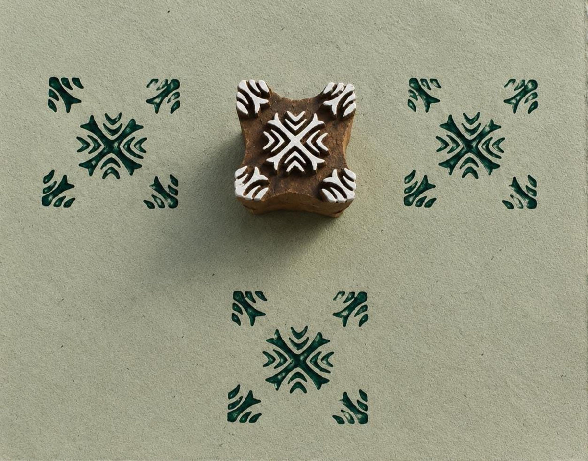 Hand carved Indian wooden printing block featuring a tribal cross geometric pattern with dark green impressions on handmade paper.