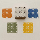 Hand carved Indian wooden textile printing block showing a repeating geometric lattice design with four curved motifs and small dots, printed in orange, blue, green and yellow.