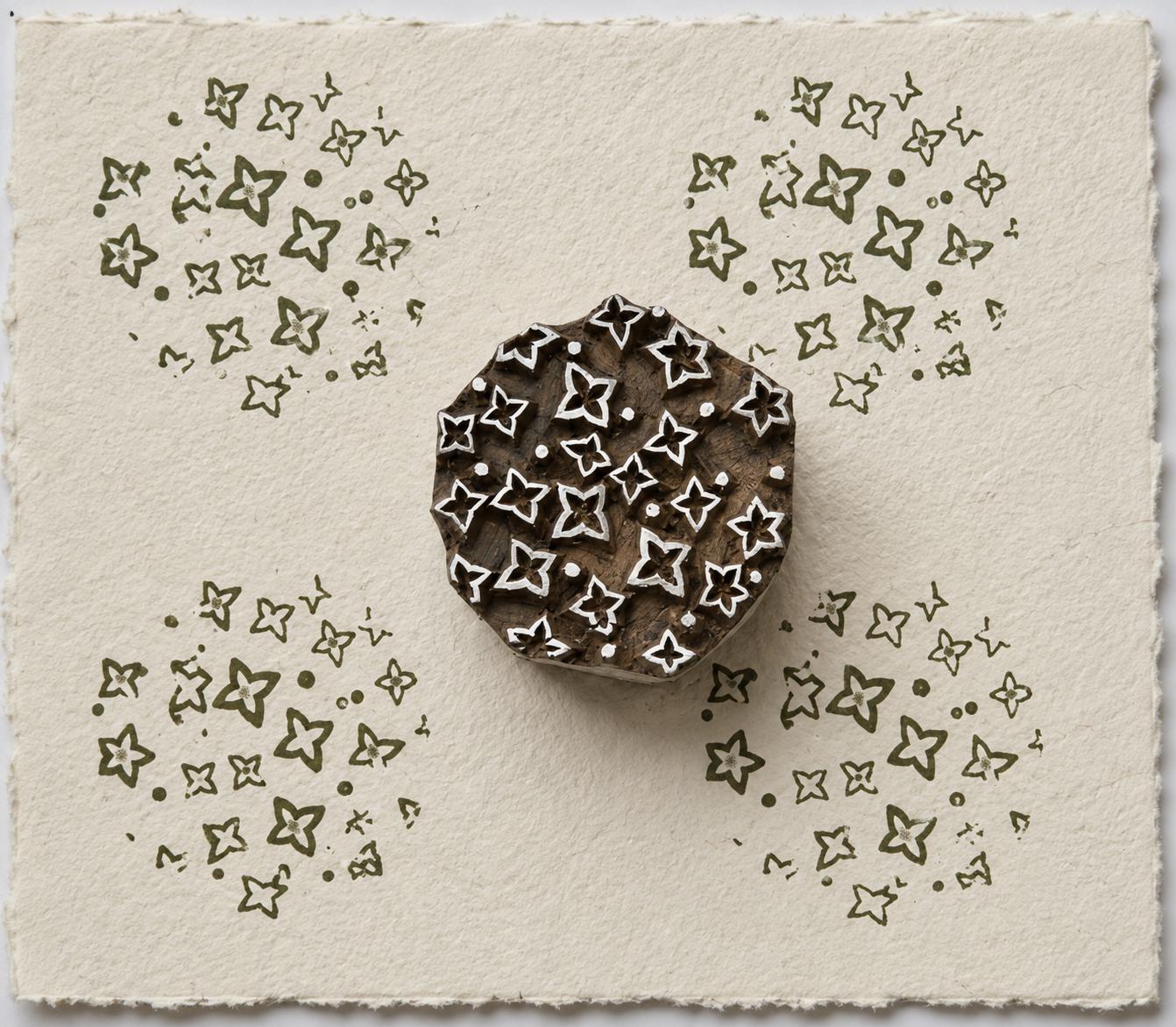 Hand carved Indian wooden printing block with a scattered folk motif of small floral and geometric shapes, shown printed on handmade paper.