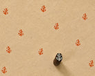 Hand carved Indian wooden printing block with a small stylized leaf motif, shown creating a repeating pattern on handmade paper.