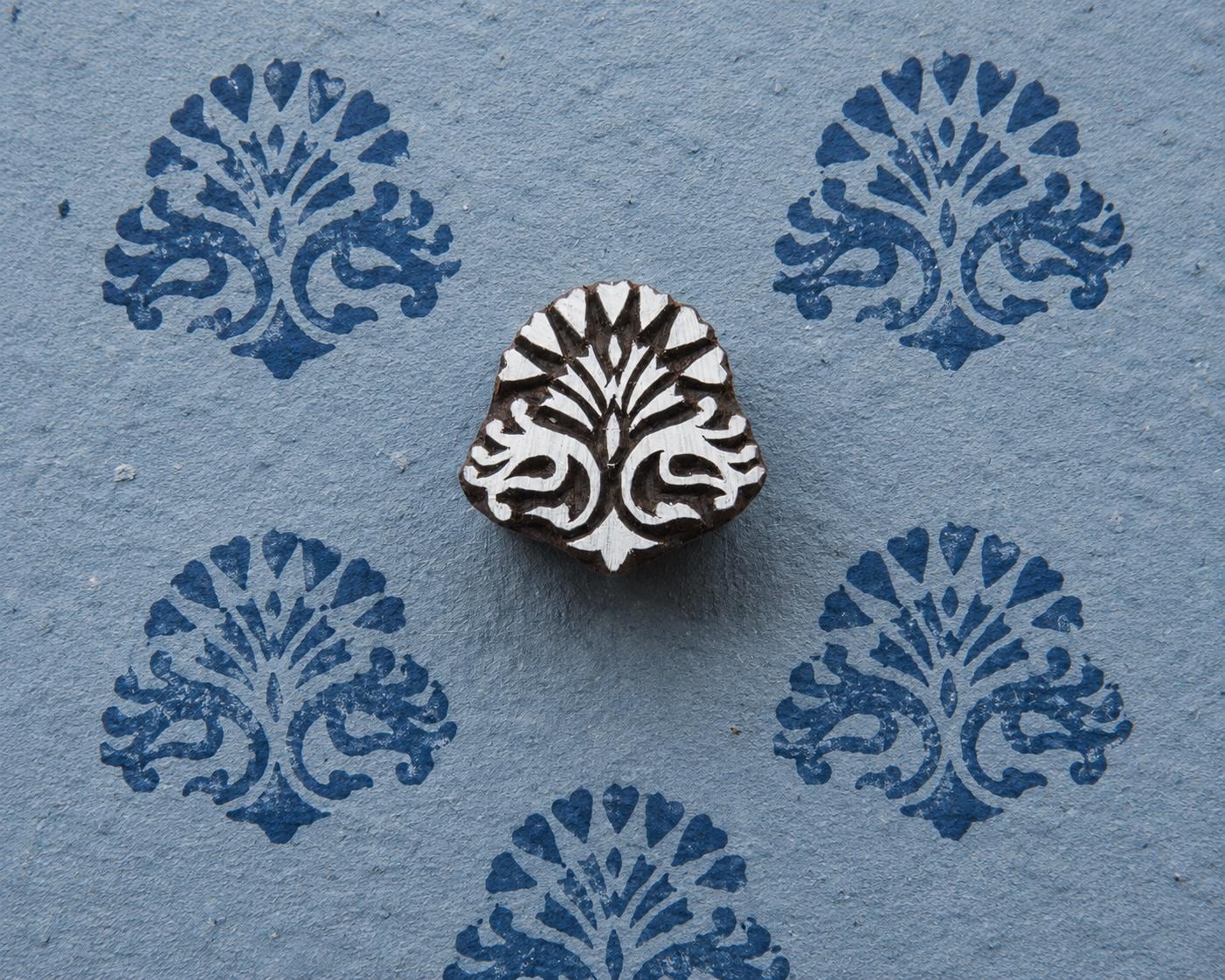 Hand-carved wooden printing block with a symmetrical traditional Indian ornamental motif, shown with blue printed impressions on textured handmade paper.