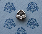 Hand-carved wooden printing block with a symmetrical traditional Indian ornamental motif, shown with blue printed impressions on textured handmade paper.