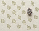 Hand-carved wooden printing block with an intricate scrolling leaf motif, shown with repeated olive-green impressions on handmade paper.