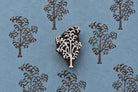 Hand-carved wooden printing block of a tree with a cascading branch and curved foliage motif, shown with repeated brown impressions on blue handmade paper.