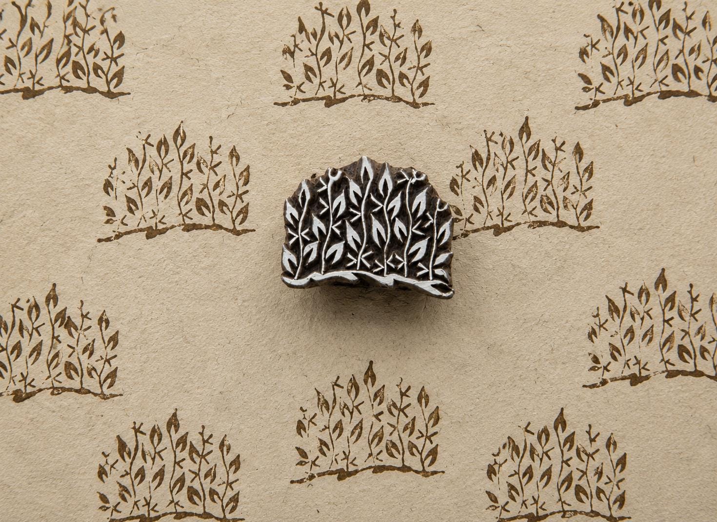 Hand-carved wooden printing block with a dense leafy branch cluster, shown with repeated brown impressions on handmade paper.
