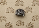 Hand-carved wooden printing block with a dense leafy branch cluster, shown with repeated brown impressions on handmade paper.