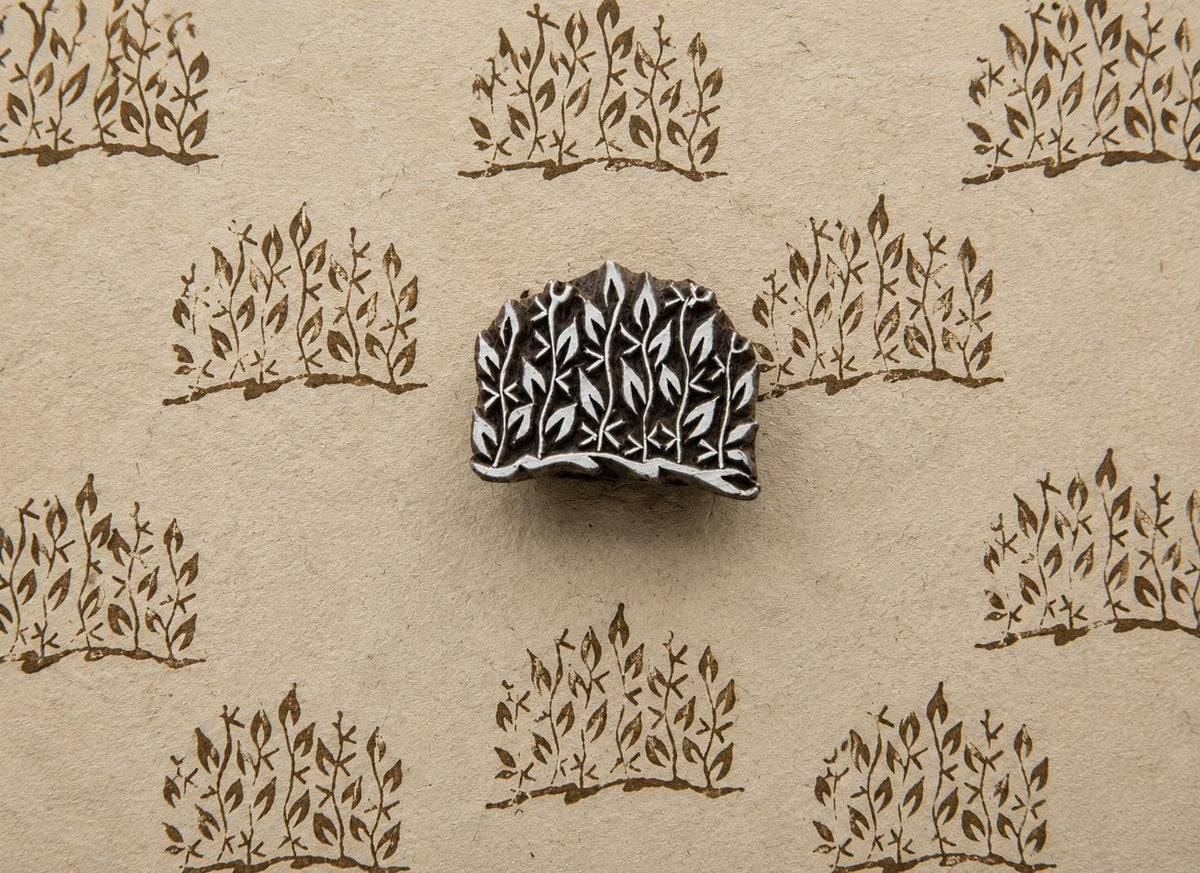 Hand-carved wooden printing block with a dense leafy branch cluster, shown with repeated brown impressions on handmade paper.