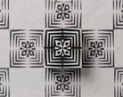 Hand carved Indian wood printing block with four-petal geometric flower and nested square border, shown with a repeating black print on handmade paper