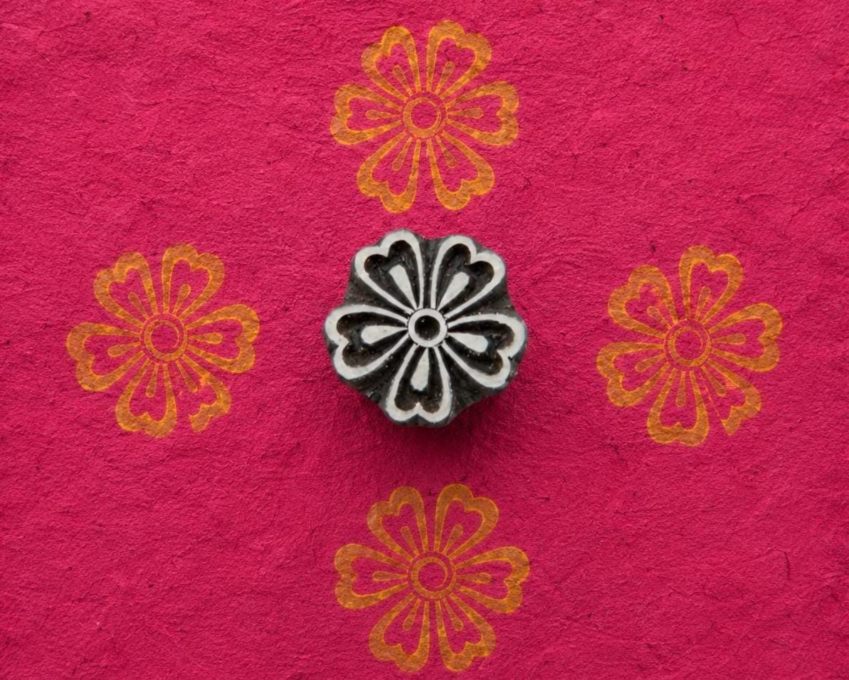 Hand carved floral wood printing block with gold flower impressions on bright pink handmade paper
