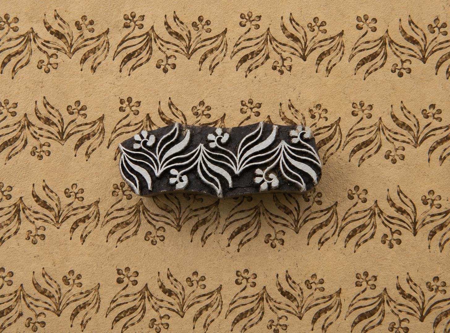Hand carved foliage border wooden printing block shown on handmade paper with a repeating brown botanical border pattern.