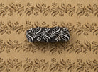 Hand carved foliage border wooden printing block shown on handmade paper with a repeating brown botanical border pattern.