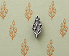 Hand carved botanical sprig wood block stamp with three flower buds, shown on handmade green paper with repeated orange botanical prints